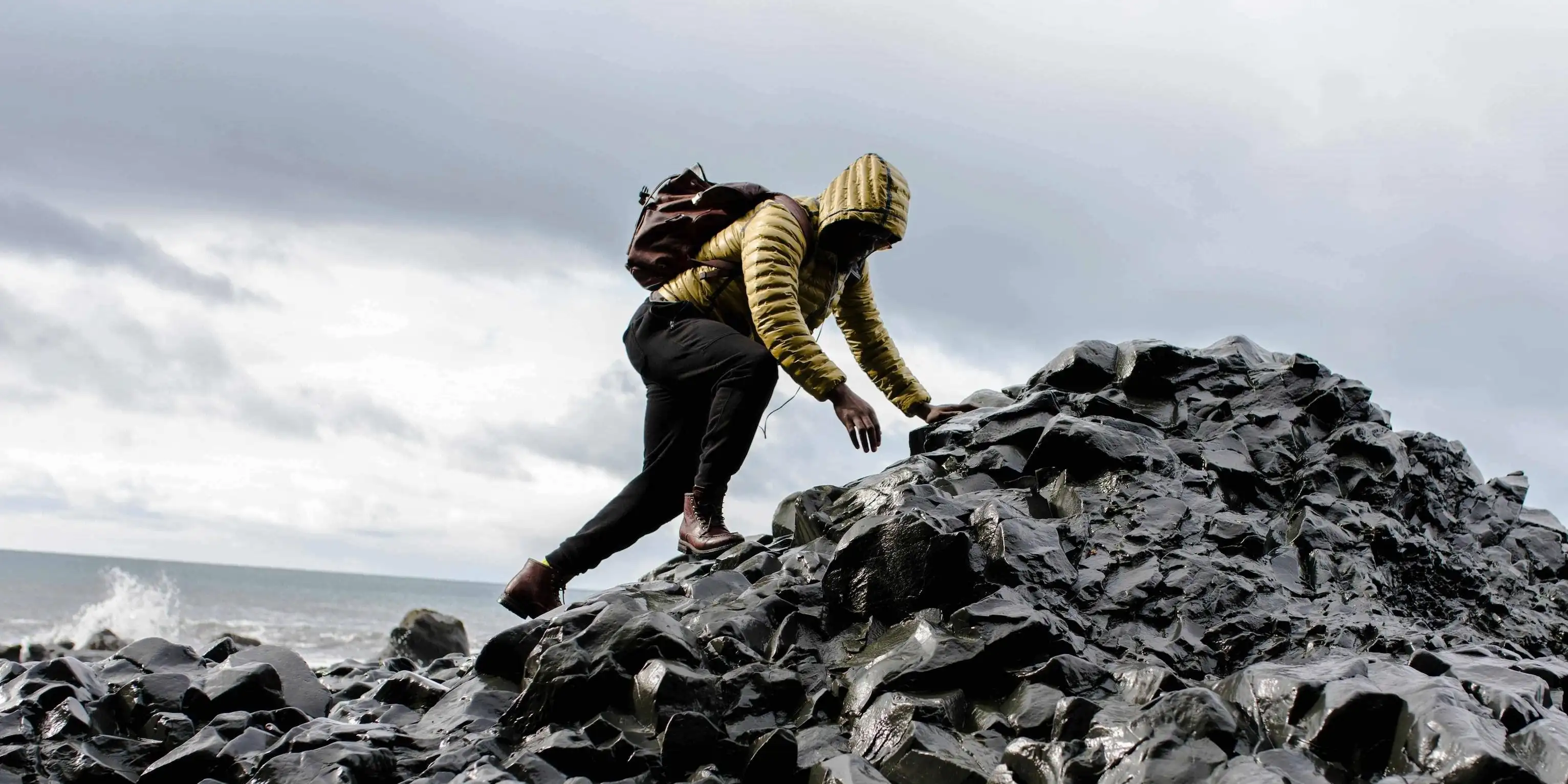 man in yellow rainjacket climbing on rocks