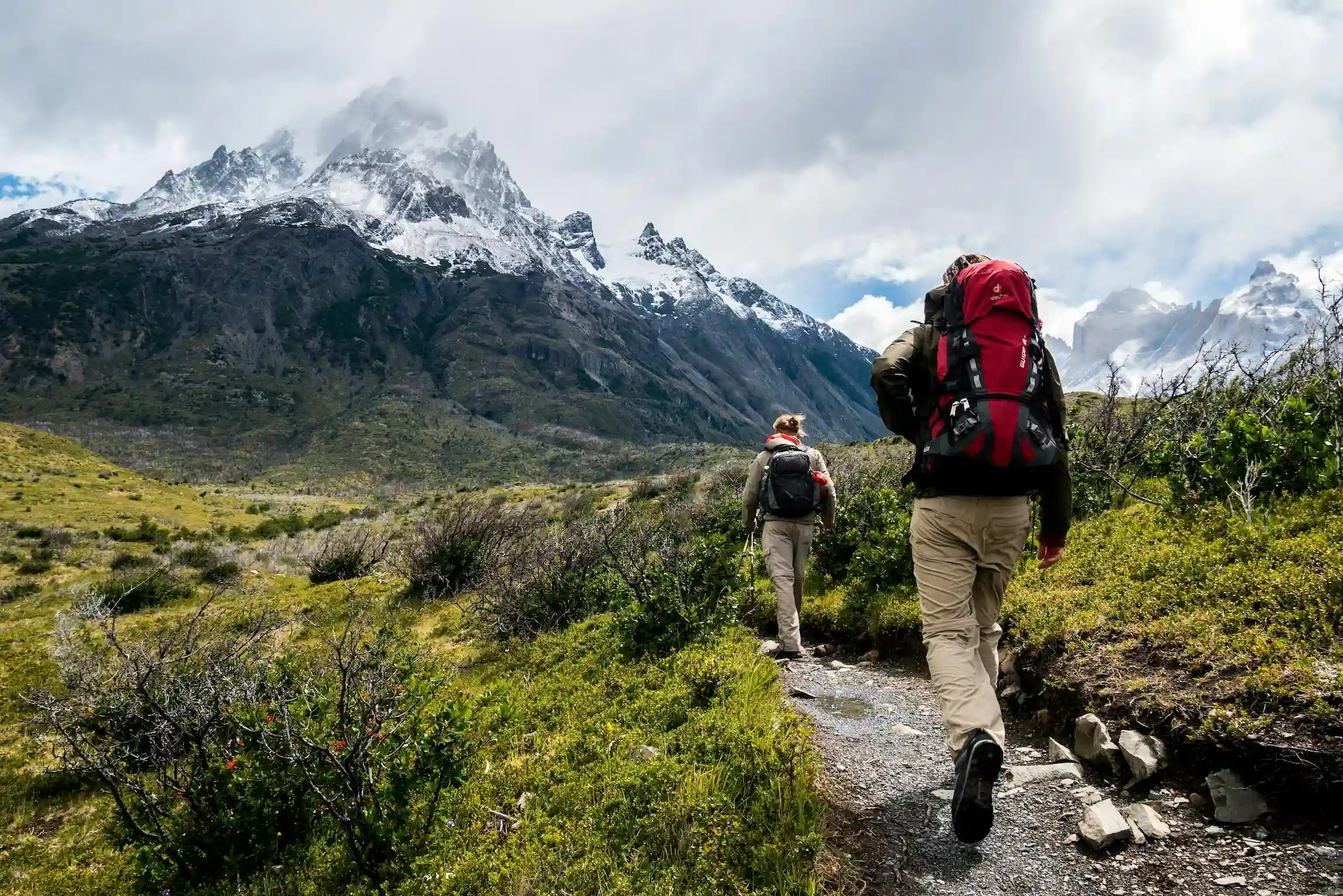two people hiking on a trail towards the mountains